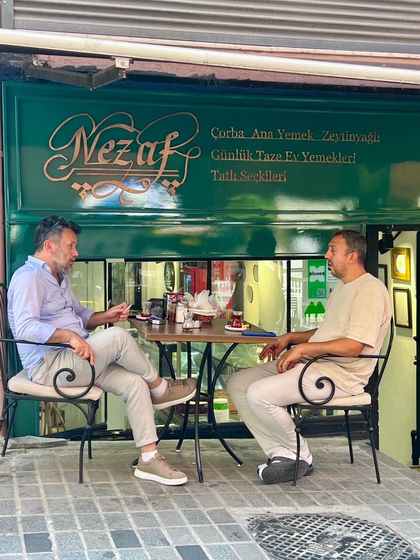 Nezaf Ev Yemekleri'nin Nişantaşı'ndaki dış cephesi, kapı önündeki masada sohbet eden iki misafir
