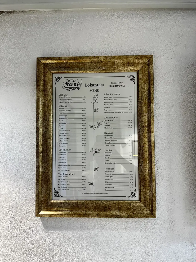 The printed menu in a gold frame on the wall at Nezaf Ev Yemekleri